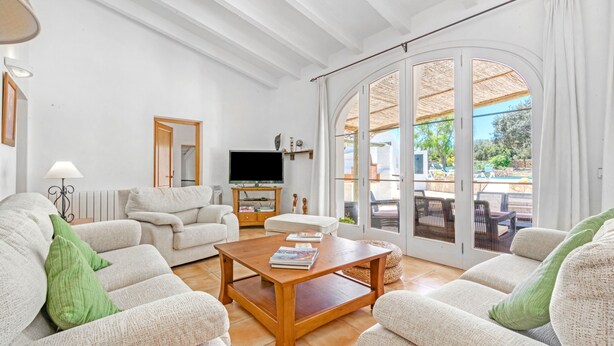 Un salón amplio con un conjunto de sofás, una mesa de centro de madera, un televisor de pantalla plana y un patio exterior accesible mediante un gran ventanal corredero.