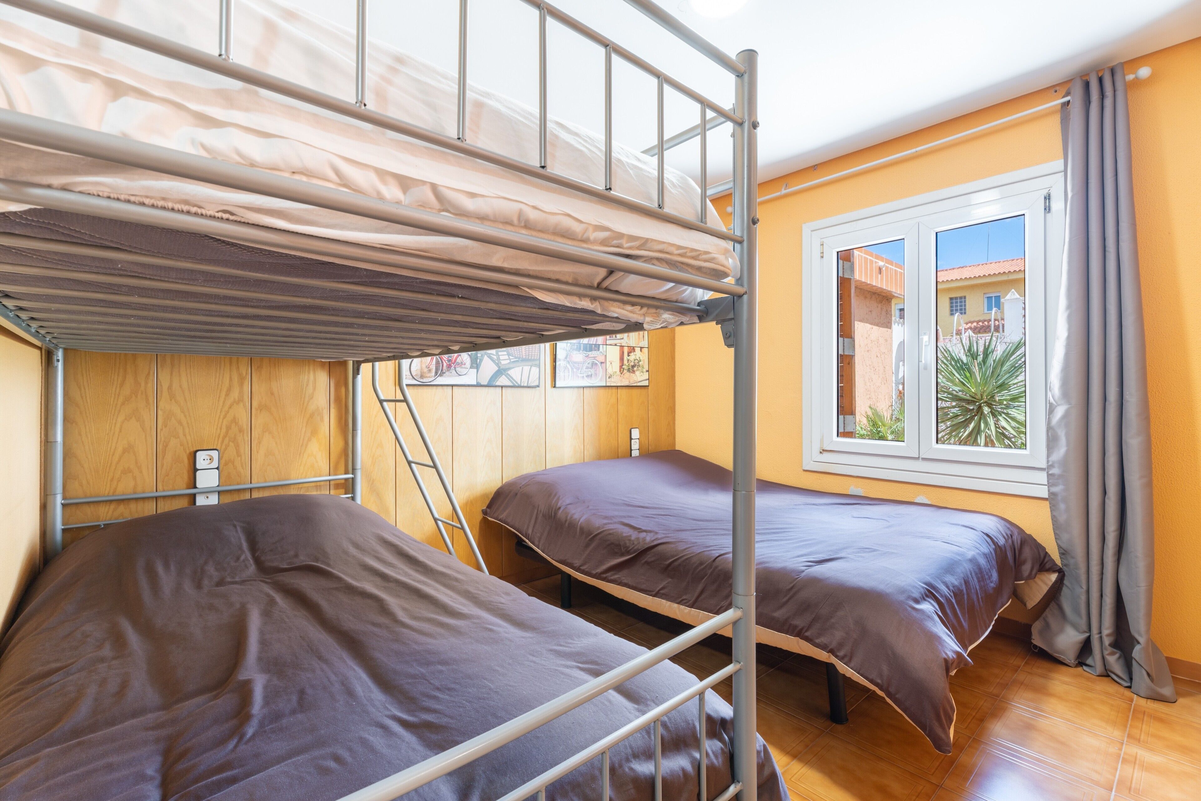 Een studentenkamer met stapelbedden, een raam met gordijnen en een uitzicht op gebouwen.