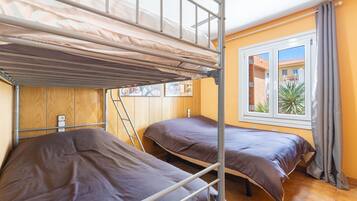 Een studentenkamer met stapelbedden, een raam met gordijnen en een uitzicht op gebouwen.