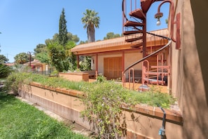 Une maison avec un escalier en colimaçon, un balcon et un jardin où poussent différentes espèces de plantes.