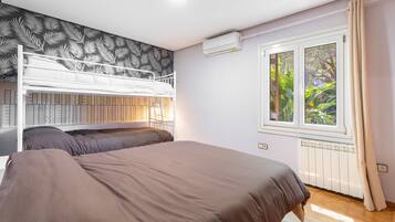 Une chambre avec des lits superposés, une fenêtre donnant sur un espace verdoyant, un appareil de climatisation et un radiateur.