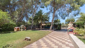 A paved pathway leading to a building with a covered entrance, surrounded by trees and a well-maintained lawn.