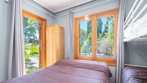 A bedroom with two beds, a wooden wardrobe, and large windows with curtains.