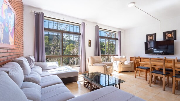 A living room with a sofa set, a glass coffee table, a dining area with wooden chairs, and a TV mounted on the wall. - Chalet 'Castellana' with Mountain View, Wi-Fi and Air Conditioning (bicorp)
