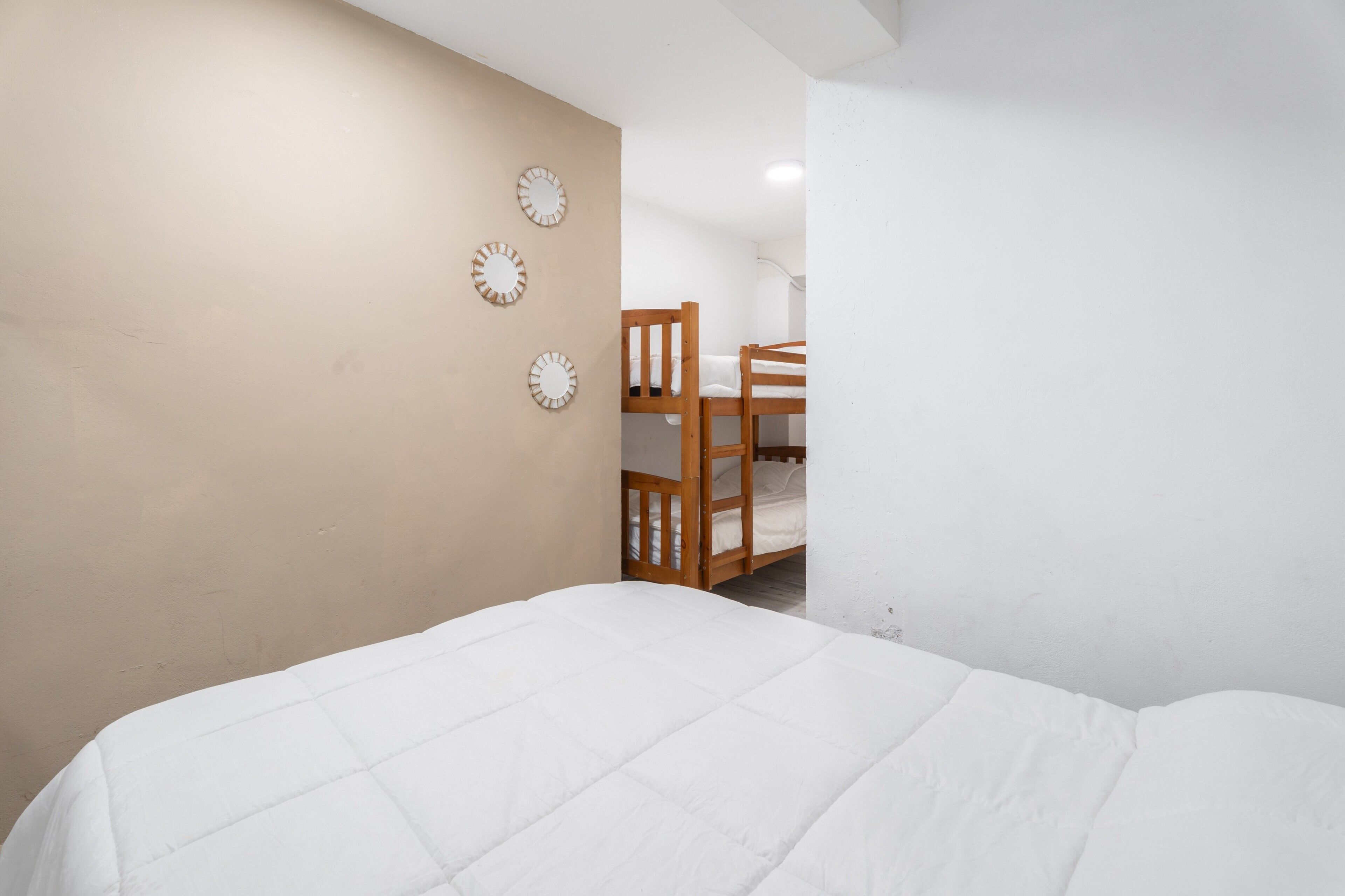 Un dormitorio con una cama litera, un edredón blanco y tres relojes de pared.