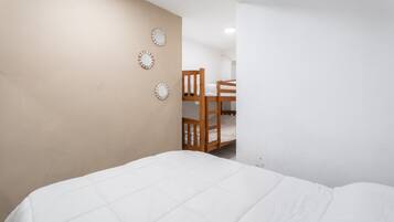 Un dormitorio con una cama litera, un edredón blanco y tres relojes de pared.