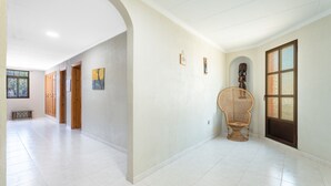 A spacious hallway with white tiled floors, wooden doors, and a rattan chair. - Chalet 'Castellana' with Mountain View, Wi-Fi and Air Conditioning (bicorp)