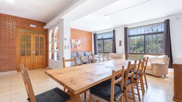 A dining area with a wooden table and chairs, a brick wall, a sofa, and large windows.