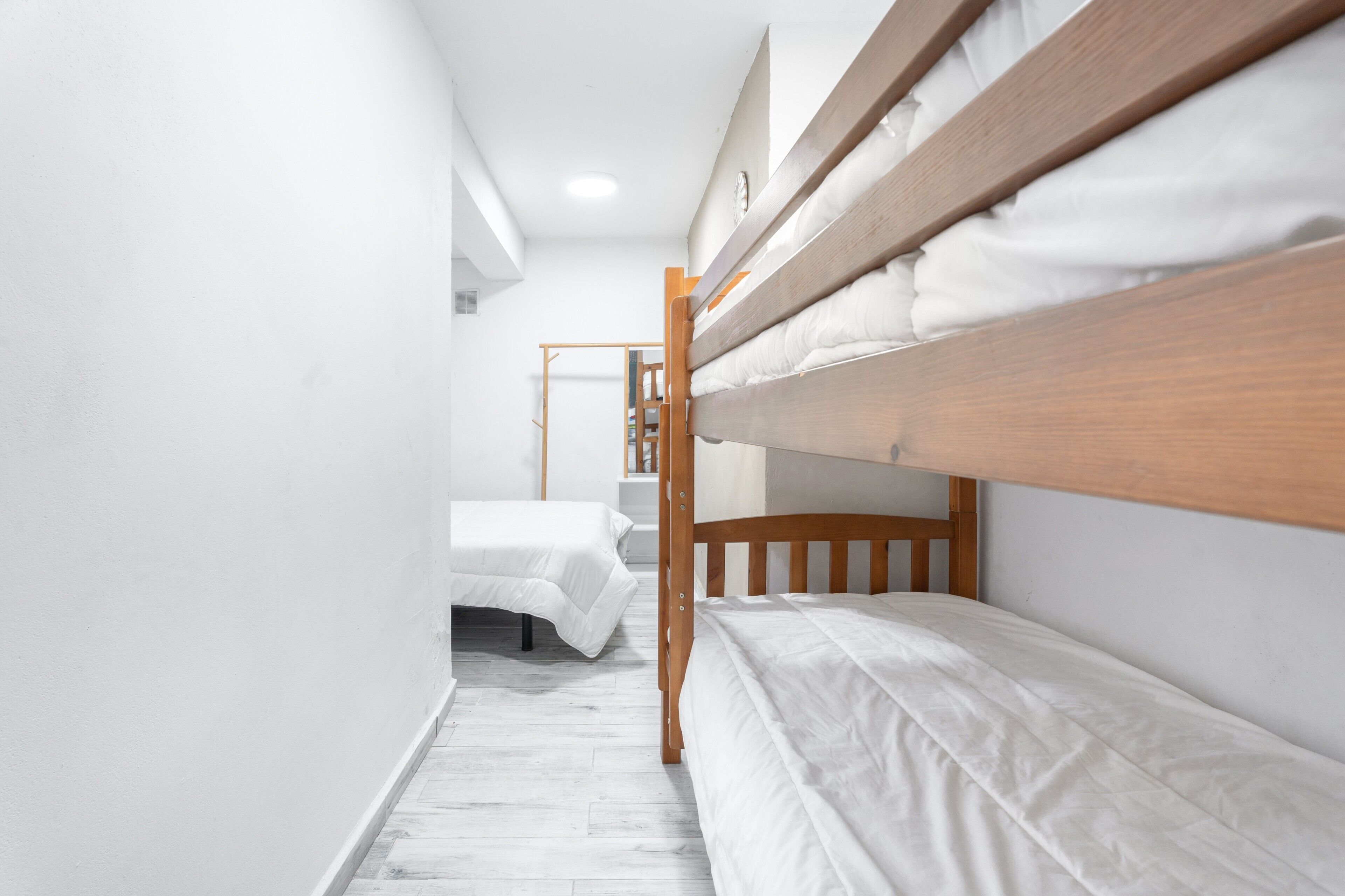 A narrow room with bunk beds, a wooden ladder, and white bedding.