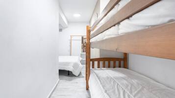 A narrow room with bunk beds, a wooden ladder, and white bedding.