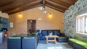 Un intérieur chaleureux avec un mur en pierre, des poutres en bois au plafond, un coin repas avec des meubles en osier et un canapé agrémenté de coussins.
