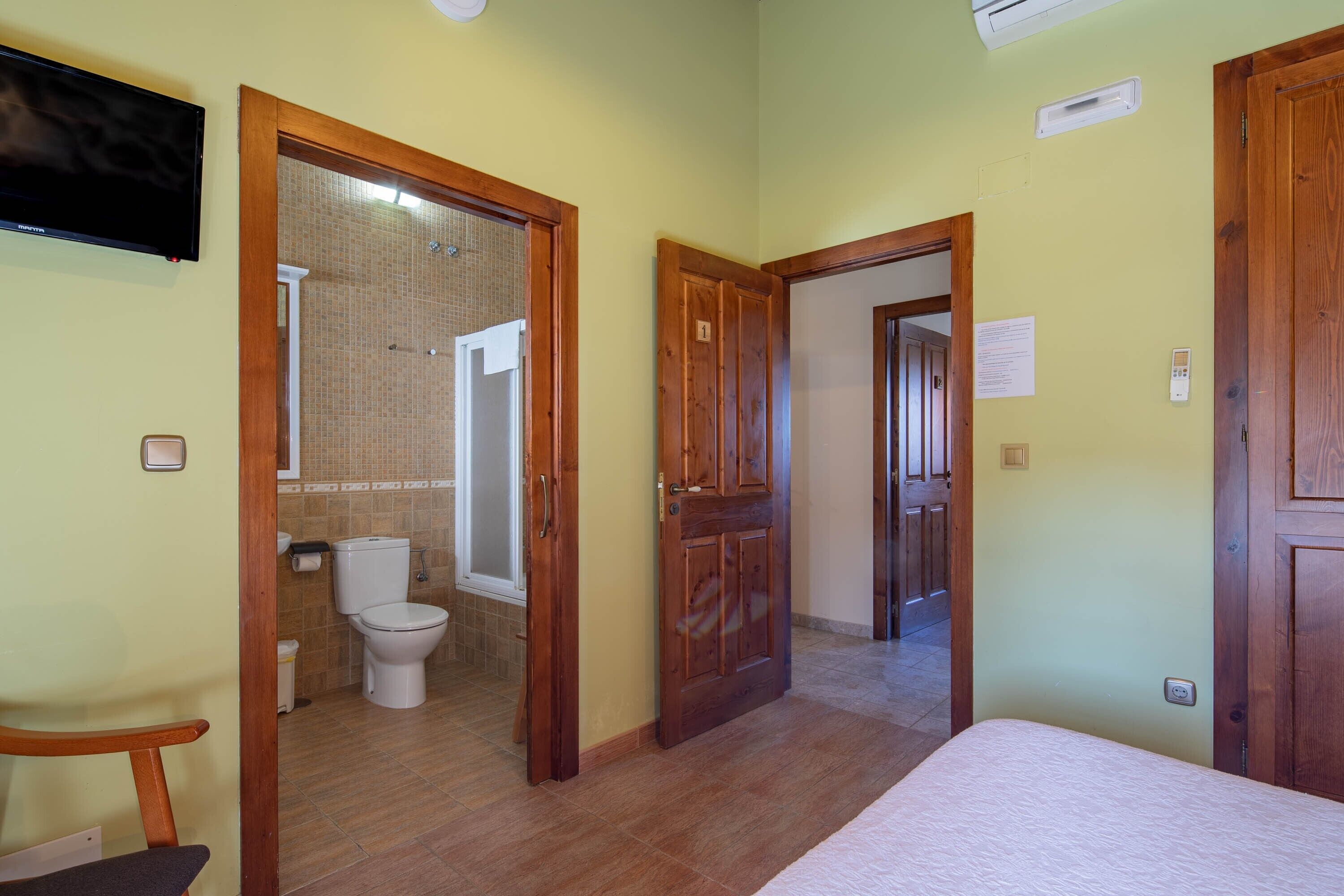 Une chambre avec un lit, une télévision, une porte en bois et une salle de bain équipée de toilettes et d’une douche.