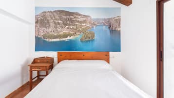 Un dormitorio con cama, mesita de noche de madera, un cuadro de un paisaje costero y una puerta.
