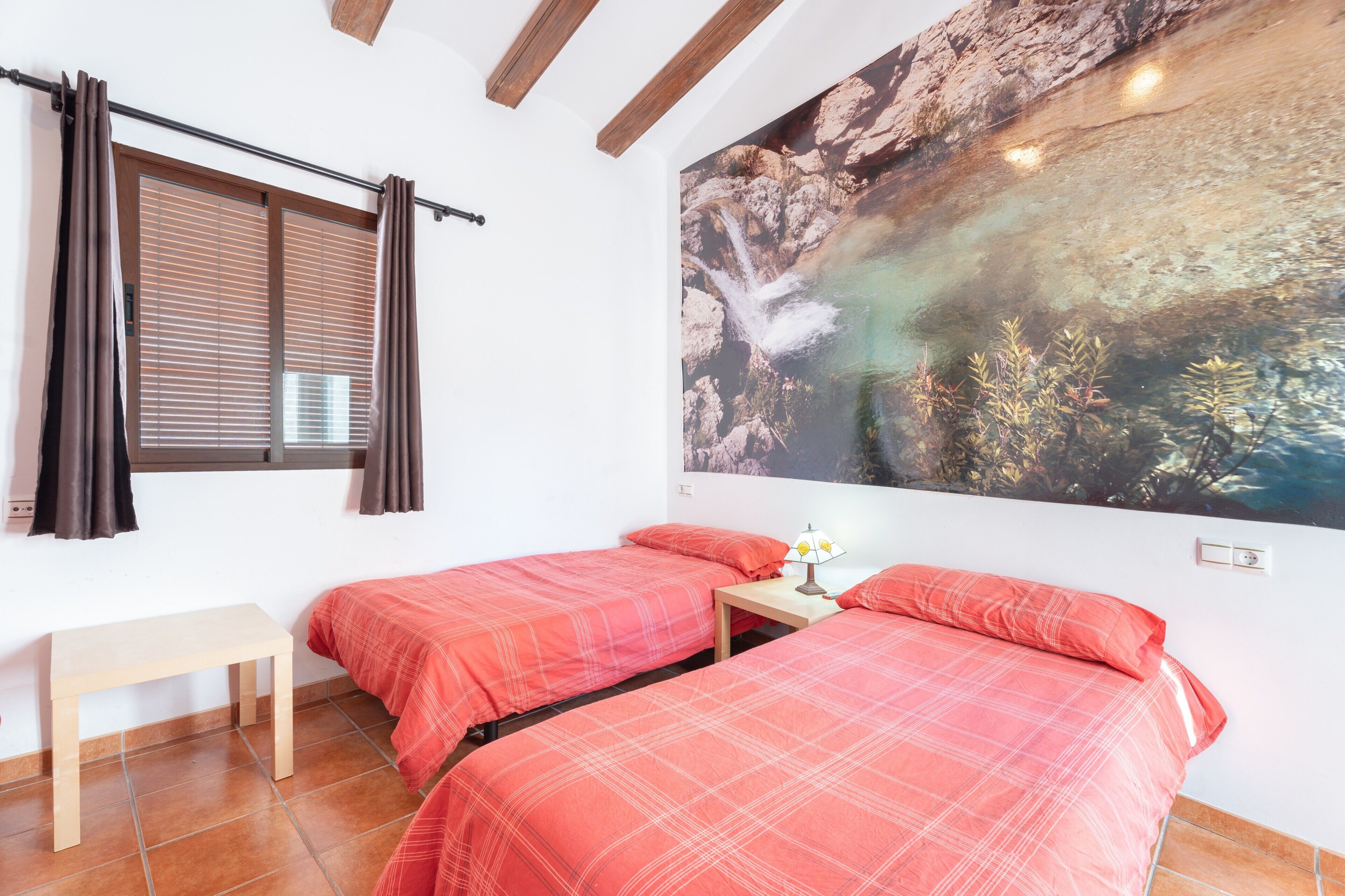 Een kamer met twee bedden, een kleine tafel, een bankje en een groot muurschilderij.