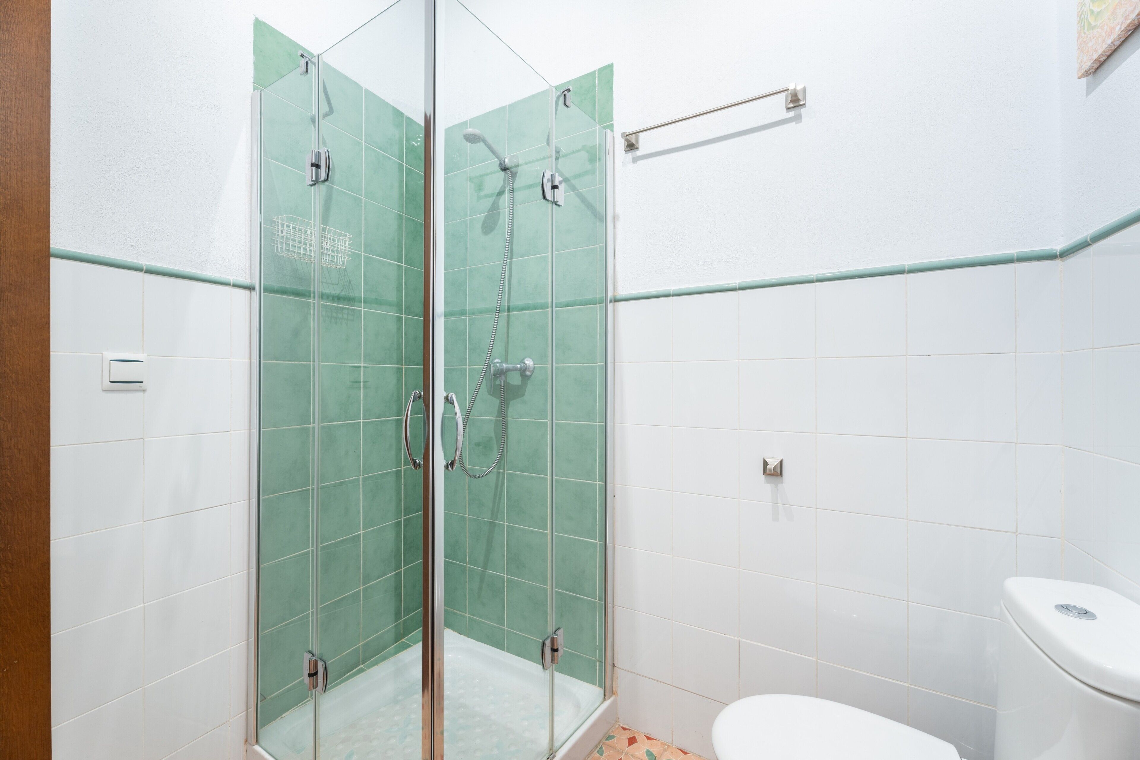 Uma casa de banho com chuveiro separado por vidro, azulejos brancos e sanita branca.