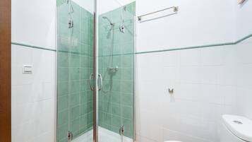 Uma casa de banho com chuveiro separado por vidro, azulejos brancos e sanita branca.