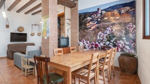 A dining area with a wooden table and chairs, a television, and a mural of a village on the wall.