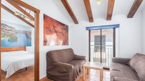 A room with a bed, two sofas, a small table, a painting, and a view of a bridge.