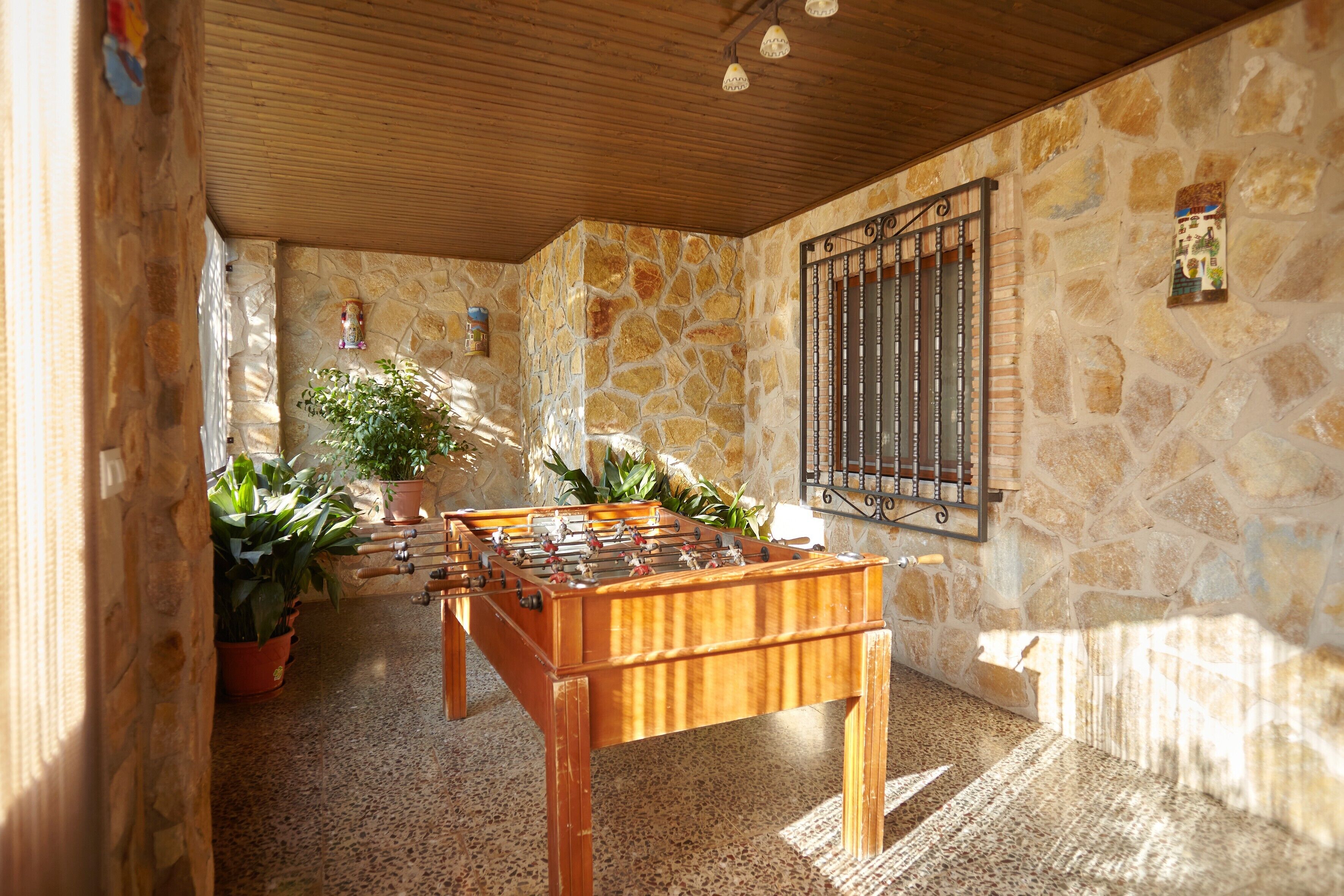 Una habitación con mesa de fútbol, paredes de piedra, techo de madera y plantas en macetas.