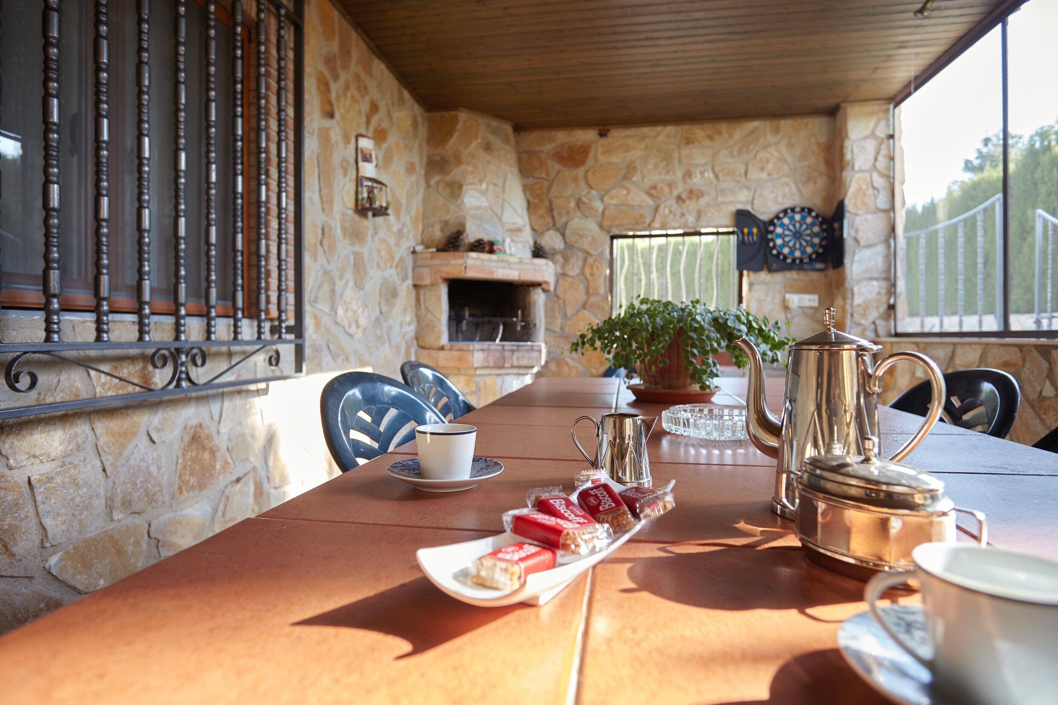 A stone-walled room with a fireplace, a table set with food and drinks, and a view of greenery outside.