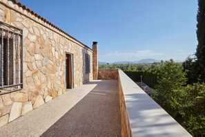 A stone building with a balcony, a stone chimney, and a view of trees and mountains.