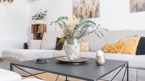 Ein modernes Wohnzimmer mit einer Glaskaraffe getrockneter Blumen auf einem Couchtisch, einer gepolsterten Couch mit gemusterten Kissen und einer Holzkabine.