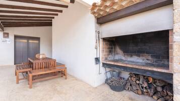 A patio with a wooden table and benches, a stone fireplace, and a door in the background.
