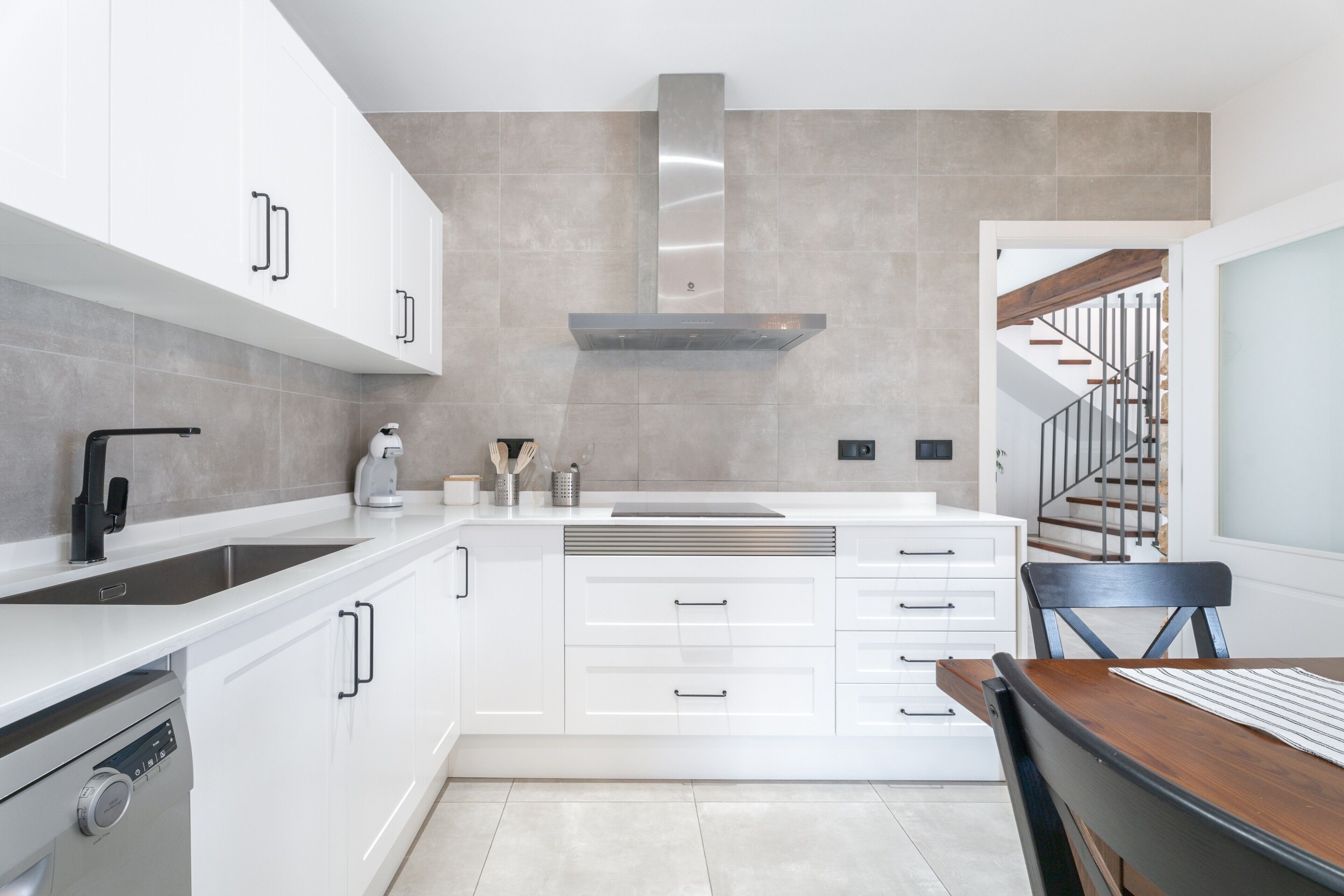 Una cocina moderna con armarios blancos, una campana extractora de acero inoxidable y un horno empotrado.