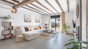 Ein modernes Wohnzimmer mit Sofa, Couchtisch und Fernseher, Holzbalken an der Decke und einer Steinwand.