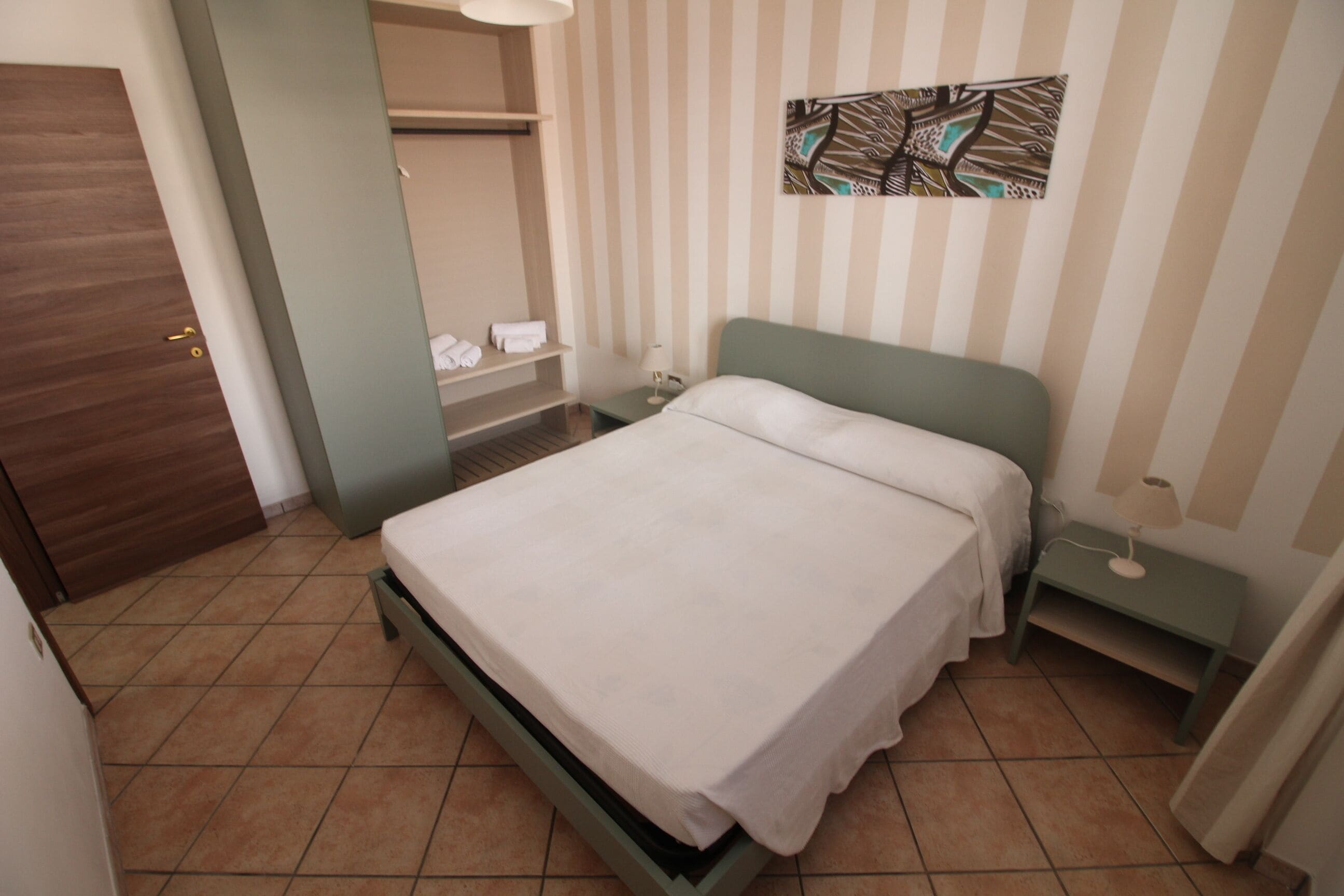 A hotel room with a bed, a nightstand, a wall-mounted artwork, and a door.