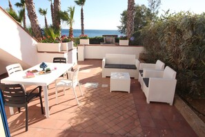 A patio with white wicker furniture, a table with a blue vase, and a view of the sea. - Residence Mare Azzurro (Ugento)