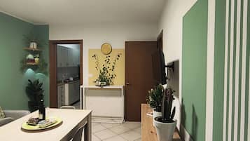 Comedor con una mesa y sillas, cocina al fondo y una pared verde con un reloj.