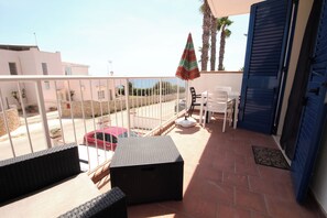 A balcony with outdoor furniture, a table, chairs, and a view of a street with cars and buildings. - Residence Mare Azzurro (Ugento)