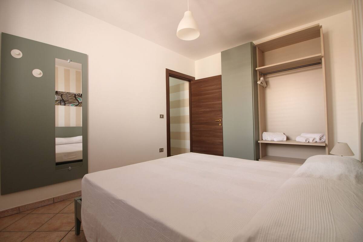 A hotel room with a bed, a wardrobe, a mirror, and a shelf with towels.