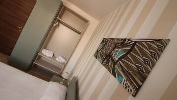 Quarto de hotel com cama, guarda-roupa, banheiro com suporte para toalhas e uma obra de arte na parede.