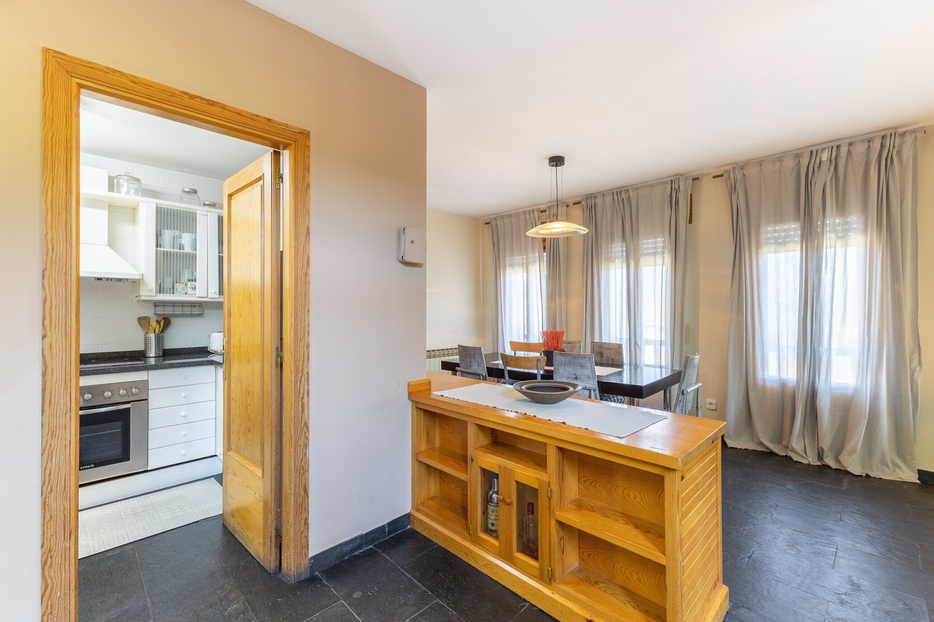 A modern kitchen with a built-in oven, a wooden island with a sink, and a dining area with a table and chairs.