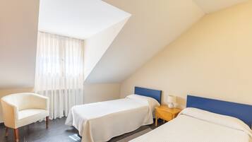 Una habitación con dos camas, una silla, una mesita de noche y una ventana con cortinas.
