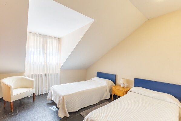 Una habitación con dos camas, una silla, una mesita de noche y una ventana con cortinas.