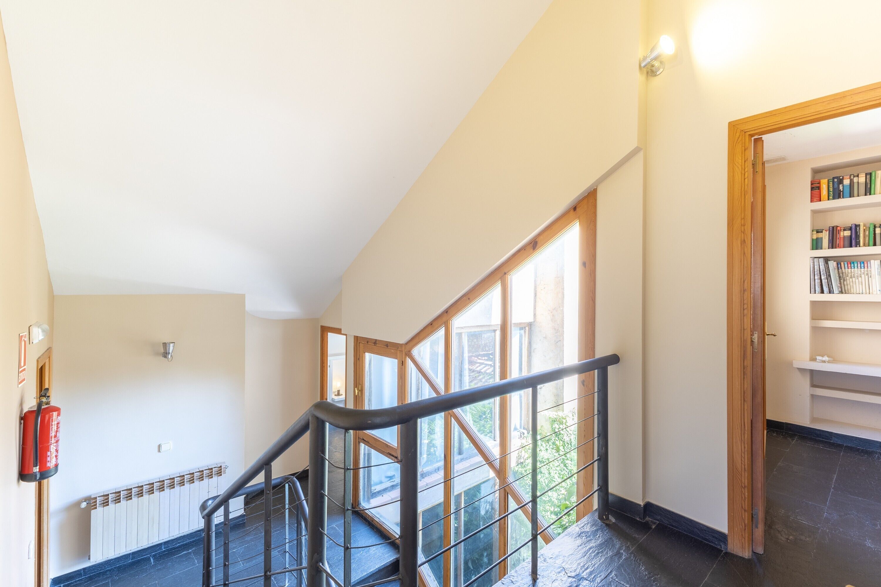 Un escalier avec des rampes en verre, un extincteur et une bibliothèque dans une pièce bien éclairée, équipée d’un radiateur.