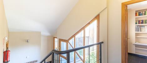 Un escalier avec des rampes en verre, un extincteur et une bibliothèque dans une pièce bien éclairée, équipée d’un radiateur.