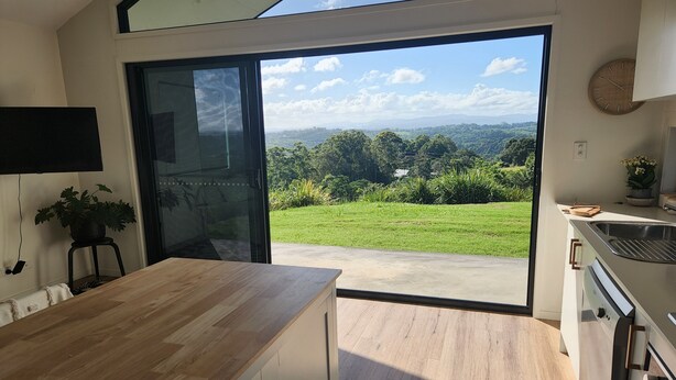 A modern kitchen with a large sliding glass door leading to a green garden. - Private Studio Byron Hinterland (Fernleigh)