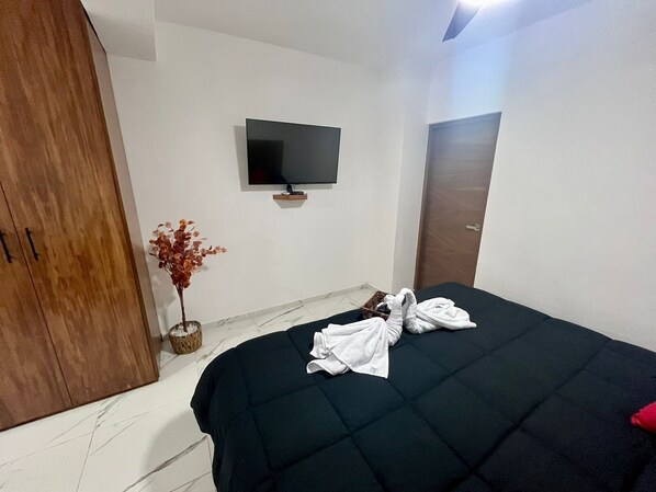 Habitación de hotel con cama, televisión montada en la pared, armario de madera y una planta pequeña.