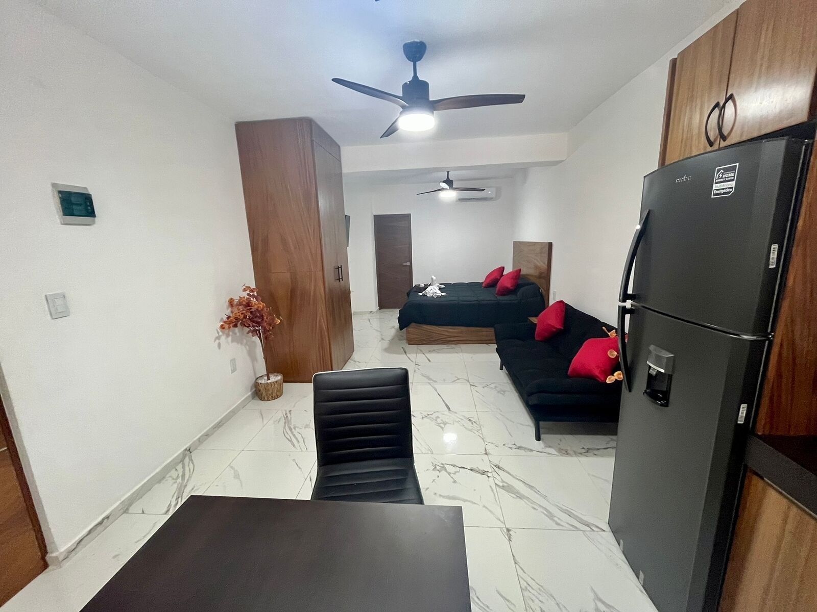 A compact living space with a dining table, two sofas, a refrigerator, and a ceiling fan.