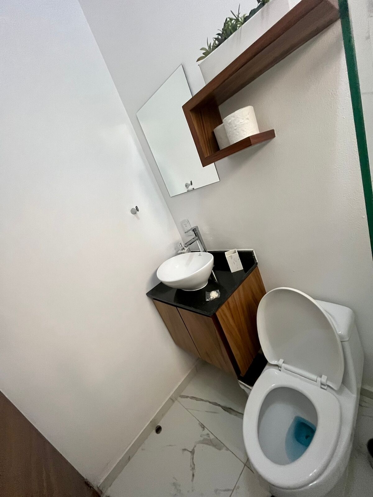 Ein modernes Badezimmer mit einem weißen Waschbecken, einer schwarzen Arbeitsplatte, einem Holflanschrank und einer weißen Toilette mit blauem Deckel.