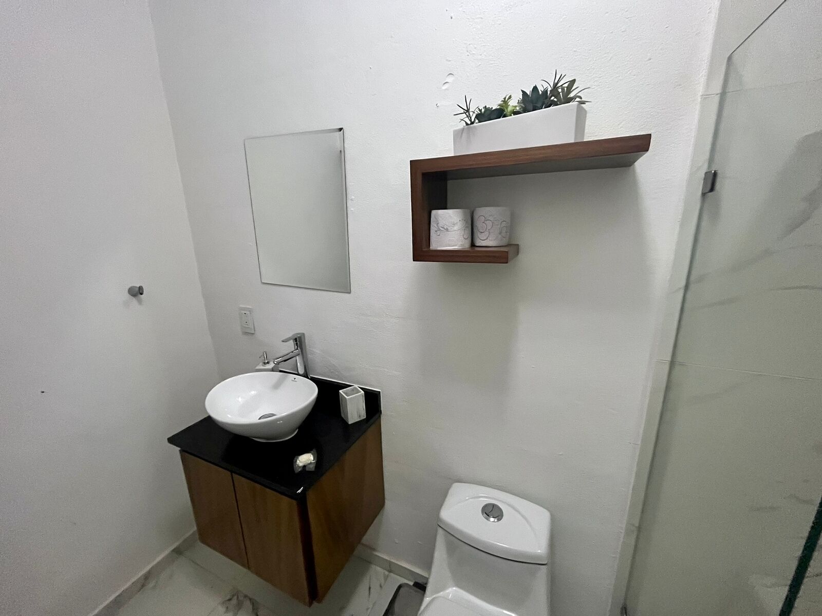 Kylpyhuone, jossa on valkoinen pesuallas, peili, wc ja hylly, jossa on hygieniatuotteita.