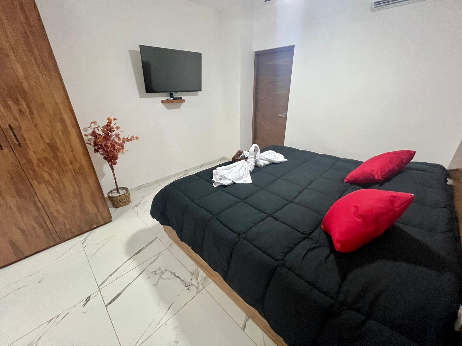 Ein Hotelzimmer mit Bett, einem an der Wand montierten Fernseher, einem Holzschrank und einer Topfpflanze.