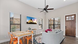 Ein geräumiges Wohnzimmer mit Essbereich, Deckenventilator und großen Fenstern mit Jalousien.