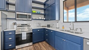 Una cocina moderna con armarios azules, electrodomésticos de acero inoxidable y un amplio ventanal que deja entrar luz natural.