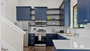 Una cocina moderna con armarios azul oscuro, un refrigerador de acero inoxidable, un microondas y una isla grande con un lavamanos.