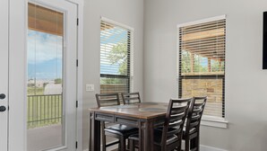 Un comedor con mesa de madera y cuatro sillas, una puerta corrediza de vidrio y una ventana con persianas.